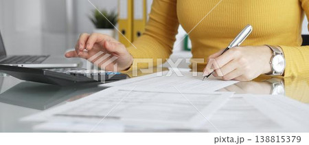 Businesswoman wearing yellow casual sweater is calculating budget and reviewing financial documents using a laptop and calculator for home finances. Audit and taxes in business Businesswoman wearing yellow casual sweater is calculating budget and reviewing financial documents using a laptop and calculator for home finances. Audit and taxes in business 138815379