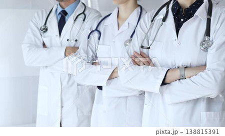 Medics from the team in white coats and with stethoscopes stand with their arms folded across their chests, embodying cohesion, professional success, and trust in the healthcare sector 138815391
