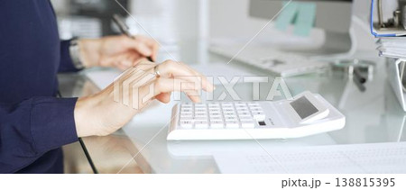 Woman using white calculator at office desk, calculating financial data for business accounting and taxes. Audit and taxes in business Woman using white calculator at office desk, calculating financial data for business accounting and taxes. Audit and taxes in business 138815395