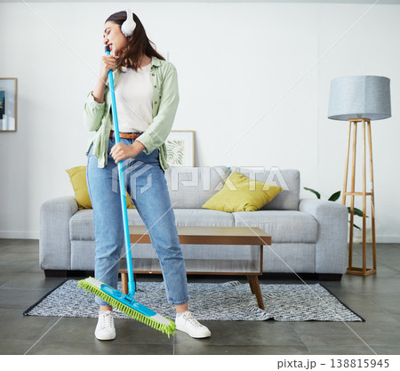 Woman, broom and singing with headphones for cleaning home, comic performance or music in living room. Girl cleaner, dancing and funny karaoke with energy, performance or streaming audio in lounge 138815945