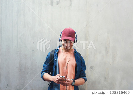 Happy, music and a man with a phone on a wall for social media, communication or a chat. Smile, technology and a male college student streaming or listening to a podcast on a mobile app with space 138816469