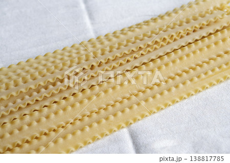 Raw Mafaldine pasta ribbons on white linen cloth. Traditional Italian wavy pasta pattern. Uncooked organic durum wheat Reginette noodles texture. Top view with copy space. 138817785