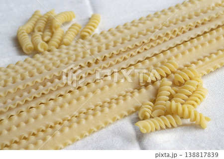 Assorted dry mafaldine and fusilli pasta on white linen tablecloth 138817839