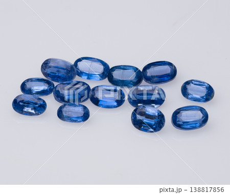 Collection of polished blue sapphire gemstones scattered on a clean white minimalist background. 138817856
