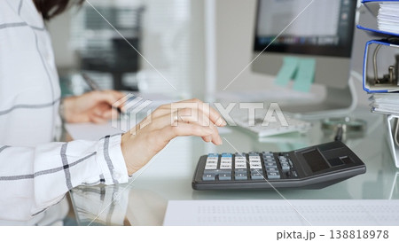 Woman calculating finances with black calculator, managing taxes, invoices, and accounting documents in office. Audit and taxes in business Woman calculating finances with black calculator, managing taxes, invoices, and accounting documents in office. Audit and taxes in business 138818978