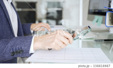 Auditor analyzing financial data with magnifying glass, scrutinizing business documents and accounting reports in office. Audit and taxes in business Auditor analyzing financial data with magnifying glass, scrutinizing business documents and accounting reports in office. Audit and taxes in business 138818987