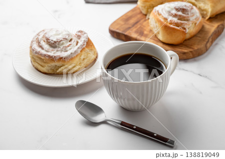 Freshly baked cinnamon rolls with white icing and a cup of black coffee on a light marble background Freshly baked cinnamon rolls with white icing and a cup of black coffee on a light marble background 138819049