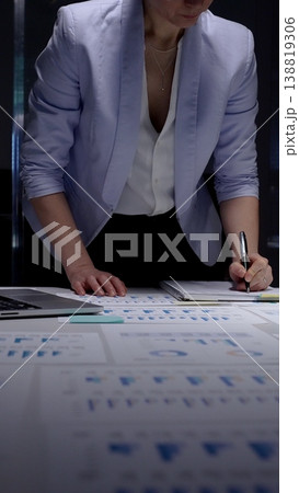 Businesswoman studying financial charts and reports on a desk late at night, analyzing data and strategy for investment, growth and corporate decision making 138819306