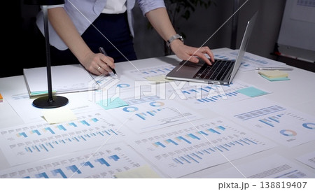 Person analyzing financial data, reviewing business analytics reports, using a laptop with charts, and planning corporate strategy with spreadsheets and investment figures 138819407