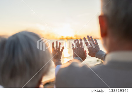 Senior couple hands at sunset. Old man woman pulls hand touching sun. Sunlight passing through fingers closeup shining sun. People stretching out hand to sun. Religion helping hand. Prayer in religion Senior couple hands at sunset. Old man woman pulls hand touching sun. Sunlight passing through fingers closeup shining sun. People stretching out hand to sun. Religion helping hand. Prayer in religion 138819543