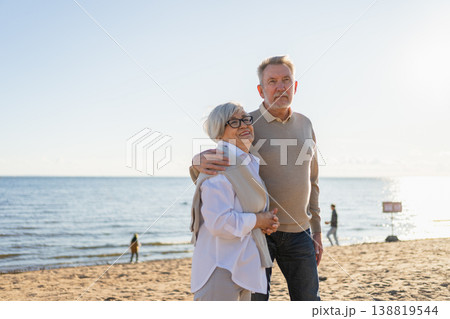Senior mature couple hugging enjoying outdoor recreation walking on beach. Old husband wife embracing with tenderness love enjoying sweet bonding. Grandmother grandfather together. Family moment love Senior mature couple hugging enjoying outdoor recreation walking on beach. Old husband wife embracing with tenderness love enjoying sweet bonding. Grandmother grandfather together. Family moment love 138819544