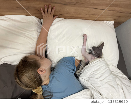 Adorable child and cat pet sleeping together in bedroom. Girl 10 years old and hairless kitten Adorable child and cat pet sleeping together in bedroom. Girl 10 years old and hairless kitten 138819630