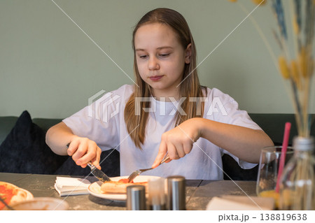 Cheerful young girl enjoying food. Child eating pizza in cafe 138819638
