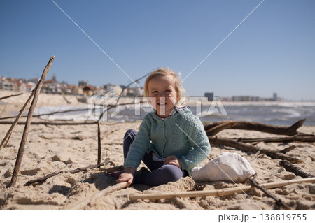 Little 4 year old girl playing with wooden sticks on a sandy beach 138819755