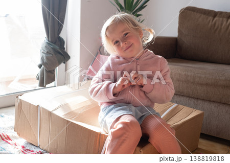 Curious 4 year old girl sitting on a huge delivery box and wondering what is inside 138819818