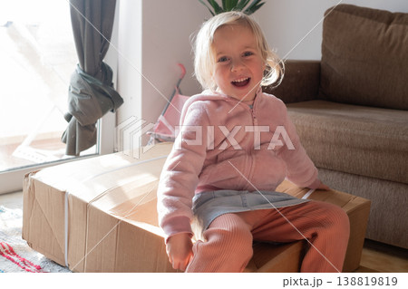 Curious 4 year old girl sitting on a huge delivery box and wondering what is inside Curious 4 year old girl sitting on a huge delivery box and wondering what is inside 138819819