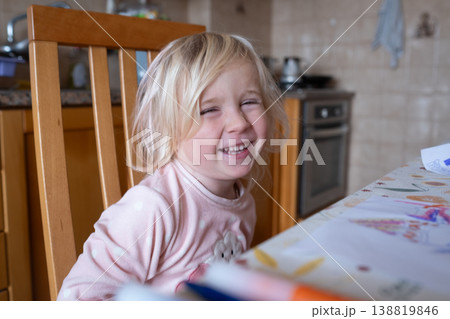 Joyful 4 year old girl smiling while sitting at a sunlit kitchen table in a cozy home Joyful 4 year old girl smiling while sitting at a sunlit kitchen table in a cozy home 138819846