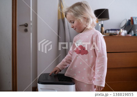 Independent 4 year old girl turning on a modern air dehumidifier to control humidity in her room Independent 4 year old girl turning on a modern air dehumidifier to control humidity in her room 138819855