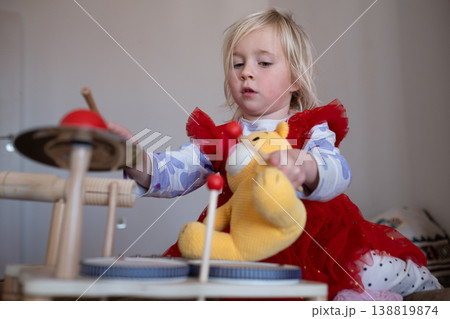 Creative 4 year old girl teaching her teddy bear to play the drums in a stylish modern playroom Creative 4 year old girl teaching her teddy bear to play the drums in a stylish modern playroom 138819874
