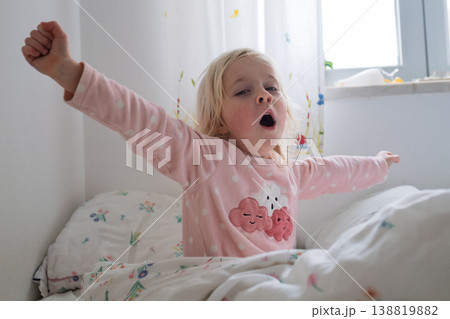 Adorable 4 year old girl yawning and stretching after waking up in a cozy sunlit bedroom 138819882