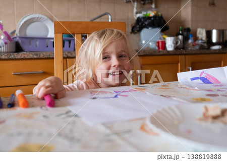 Joyful 4 year old girl smiling while sitting at a sunlit kitchen table in a cozy home 138819888