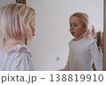 Funny little girl making faces in front of the mirror. 138819910