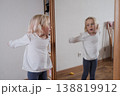 Funny little girl making faces in front of the mirror. 138819912