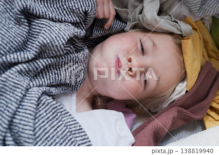 Funny child peeking out from a heap of laundry and laughing. 138819940