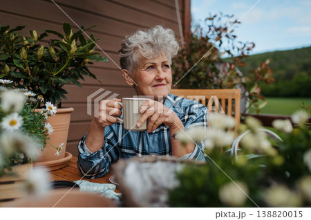 Senior woman with coffee sitting on terrace, resting after gardening. Senior woman with coffee sitting on terrace, resting after gardening. 138820015