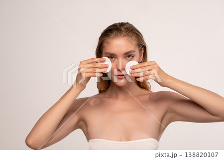 Young woman completing daily skincare routine with cotton pads, cleansing and refreshing her face Young woman completing daily skincare routine with cotton pads, cleansing and refreshing her face 138820107