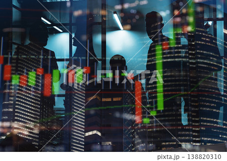 Business people discuss financial charts at night inside an office building with city lights in the background Business people discuss financial charts at night inside an office building with city lights in the background 138820310