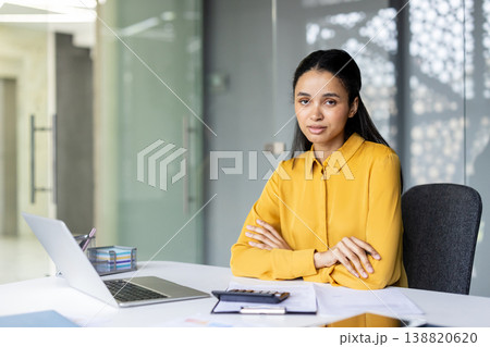 Young woman sitting at a desk with arms crossed, working in a contemporary office environment, embodying professionalism, entrepreneurship, and career success Young woman sitting at a desk with arms crossed, working in a contemporary office environment, embodying professionalism, entrepreneurship, and career success 138820620