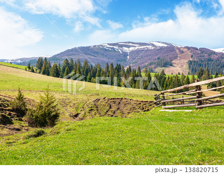 mountainous countryside landscape in spring. wooden fence and grassy meadow on a green hill. distant mountain ridge with snow capped tops. sunny weather with blue sky. natural carpathian image mountainous countryside landscape in spring. wooden fence and grassy meadow on a green hill. distant mountain ridge with snow capped tops. sunny weather with blue sky. natural carpathian image 138820715