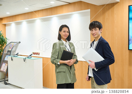 企業の受付でノートPCと手帳を持ち笑顔で並ぶ男女のビジネスパーソン 企業の受付でノートPCと手帳を持ち笑顔で並ぶ男女のビジネスパーソン 138820854