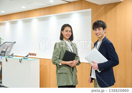 企業の受付でノートPCと手帳を持ち笑顔で並ぶ男女のビジネスパーソン 138820860