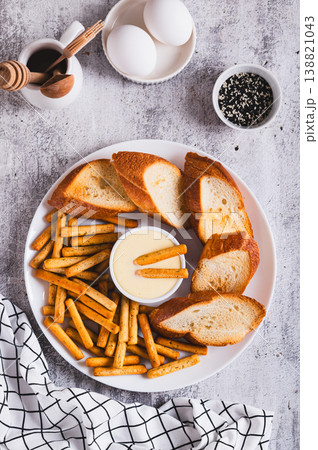 Hollandaise sauce with breadsticks and toast on a plate on the table top and vertical view Hollandaise sauce with breadsticks and toast on a plate on the table top and vertical view 138821043