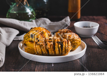 Baked Hasselback potatoes with cheese, garlic and herbs on a plate on the table Baked Hasselback potatoes with cheese, garlic and herbs on a plate on the table 138821064