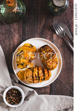 Crispy baked accordion potatoes with cheese and herbs on a plate top and vertical view 138821070