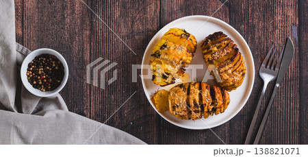 Crispy baked accordion potatoes with cheese and herbs on a plate top view web banner 138821071