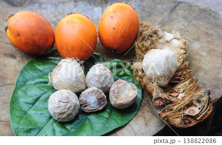 Collection of orange and green betel nuts with broken betel nut shells placed on a textured wooden surface. Collection of orange and green betel nuts with broken betel nut shells placed on a textured wooden surface. 138822086