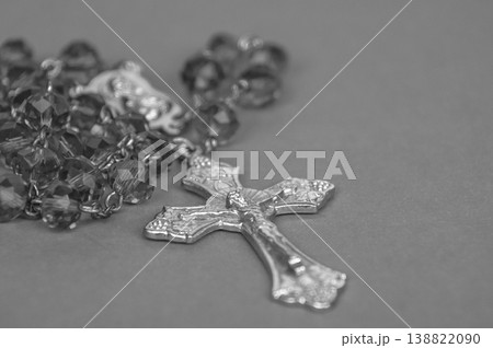 Monochrome Rosary with metallic crucifix and reflective beads displayed on neutral background in a dramatic black and white religious still life. 138822090