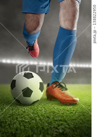 Action close-up of a professional soccer player in blue kit and orange cleats about to kick a ball on a green pitch in a floodlit stadium at night 138822950
