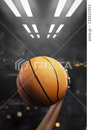 A basketball held aloft by a player's hand in a dark arena with dramatic spotlights and bokeh background, symbolizing the start of a game or a winning moment A basketball held aloft by a player's hand in a dark arena with dramatic spotlights and bokeh background, symbolizing the start of a game or a winning moment 138822952