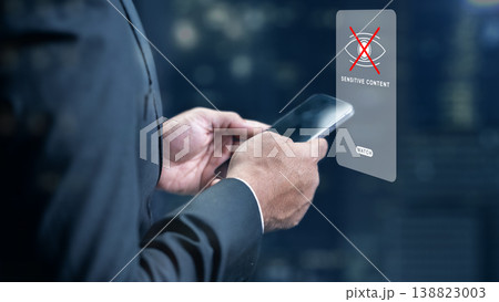 Professional man holding a smartphone with a digital holographic sensitive content warning icon, illustrating data privacy, internet safety, and content moderation policies Professional man holding a smartphone with a digital holographic sensitive content warning icon, illustrating data privacy, internet safety, and content moderation policies 138823003