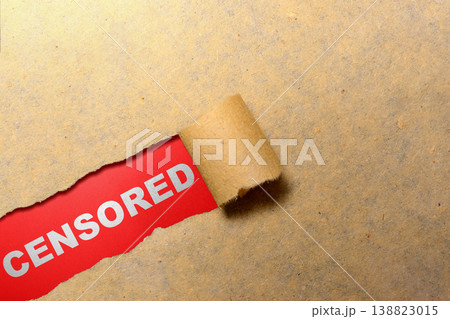 A piece of brown paper is torn open to reveal the white word CENSORED on a vibrant red background, symbolizing restricted information and media control 138823015