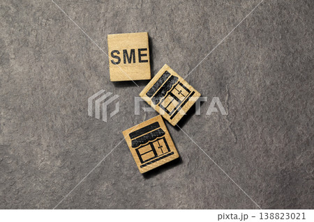 SME business concept featuring three wooden blocks with the acronym SME and storefront icons laid flat on a dark textured stone surface, representing small and medium enterprises 138823021