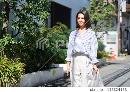 買い出しの帰り道、スマホを片手に笑顔で休日の散歩を楽しむ日本人女性。 138824188