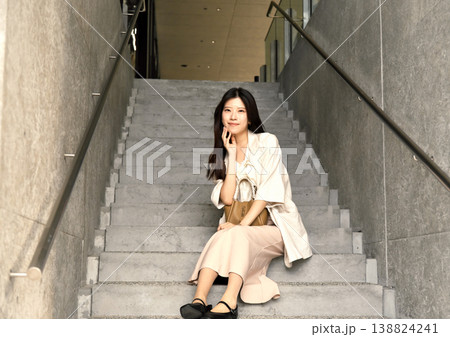 大阪・梅田の近代的な階段に座る、黒ニットとベージュパンツのクールな女性 大阪・梅田の近代的な階段に座る、黒ニットとベージュパンツのクールな女性 138824241