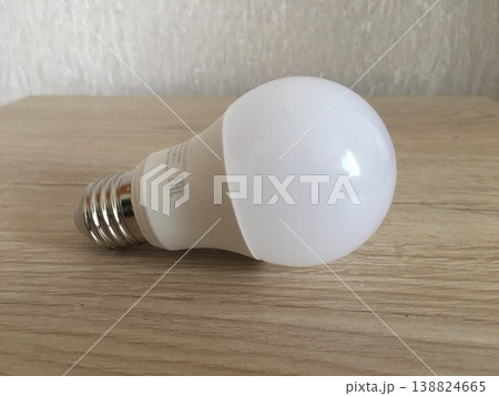 Light bulb resting on wooden surface in a well-lit room showing basic design and structure of common household item 138824665