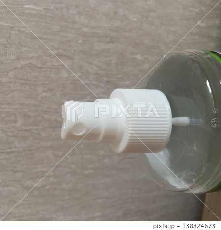 Clear plastic bottle with a white pump dispenser sitting against a textured wall in a well-lit room 138824673